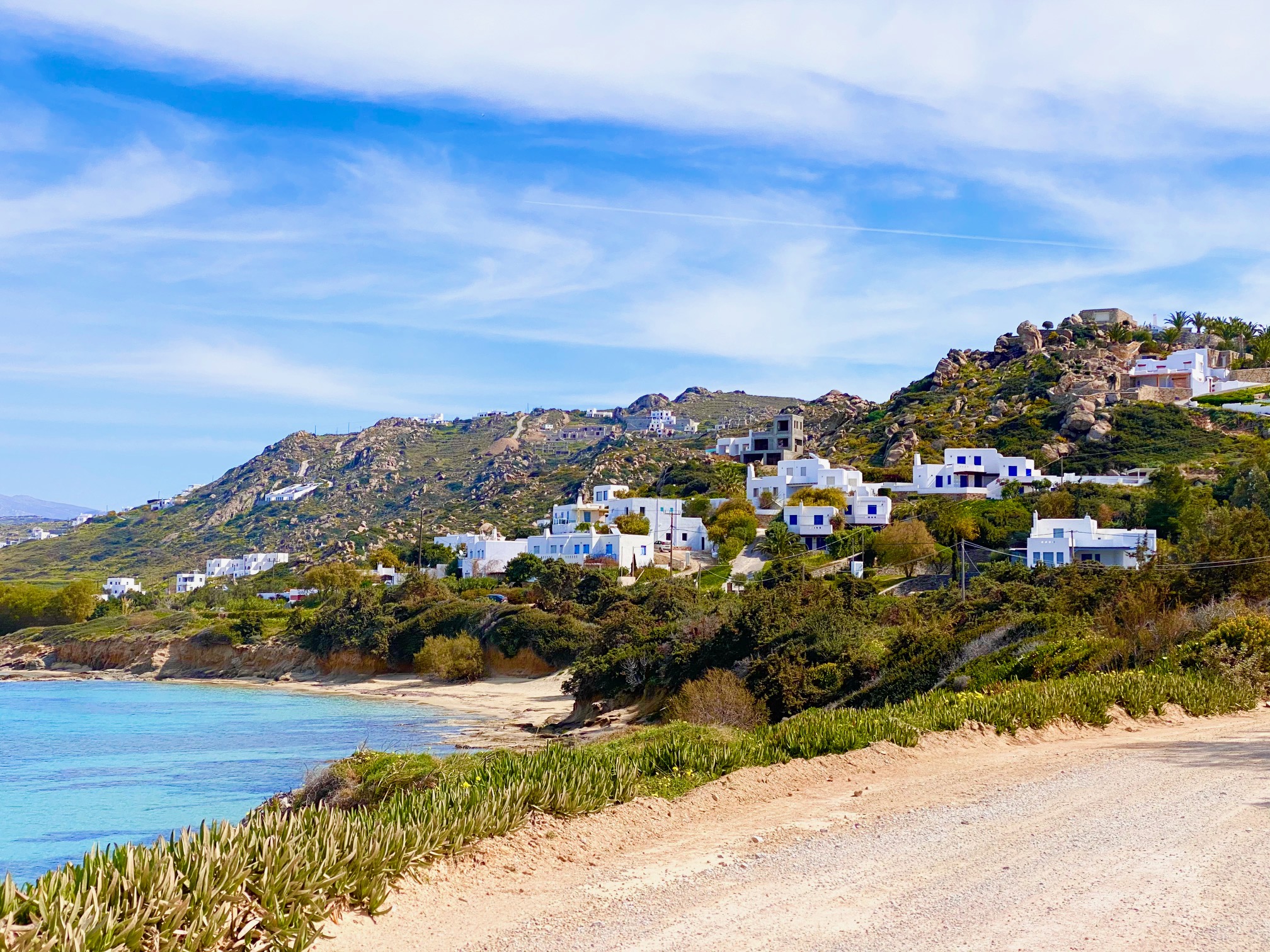 View of dirt road with the sea, beach and villas beyond | Should I Rent a Car in Naxos? | greekislandbucketlist.com