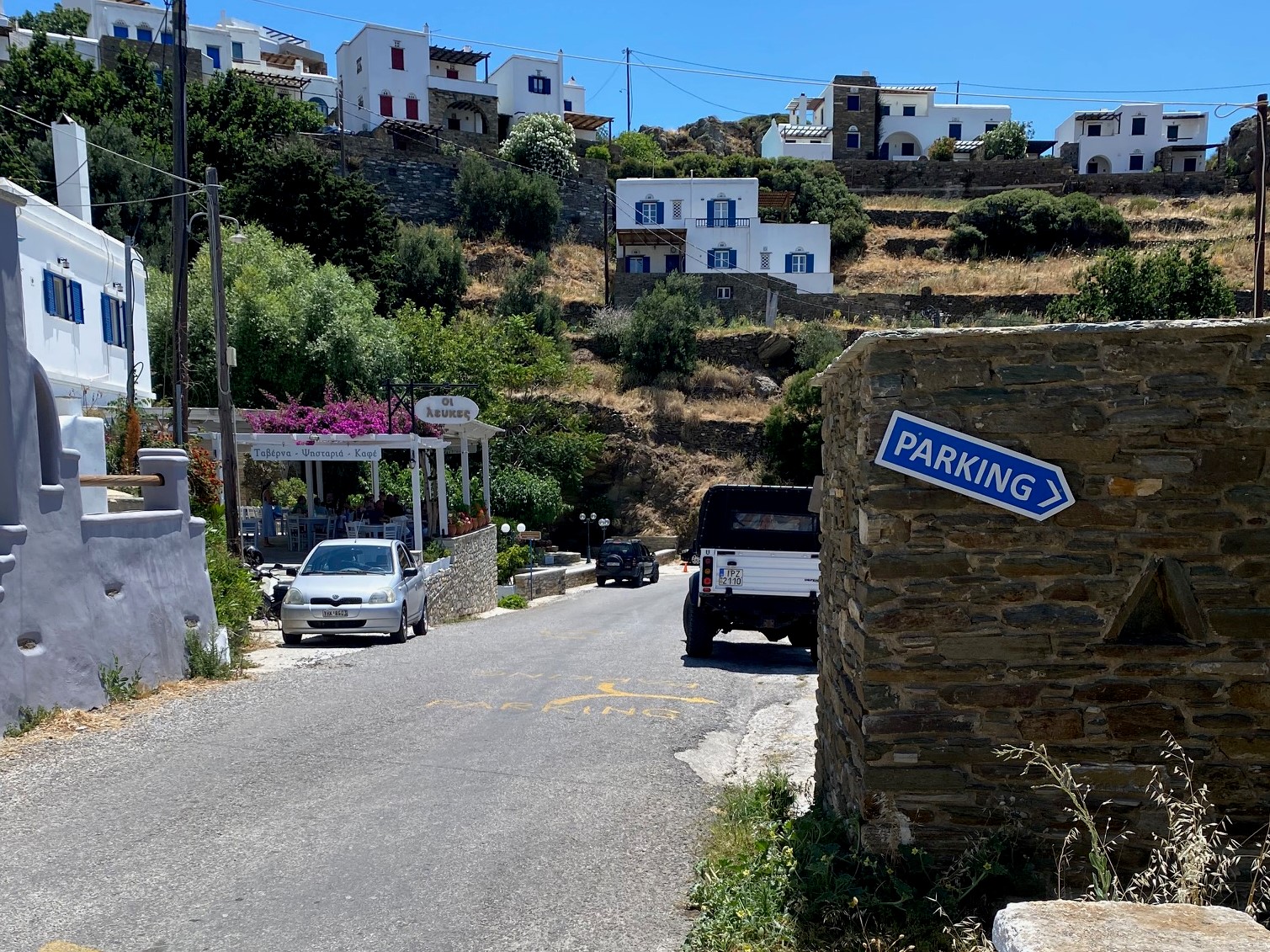 A road through a traditional Greek village with a sign to parking | Hiring a Car in Greece for Greek Island Hopping - Greekislandbucketlist.com