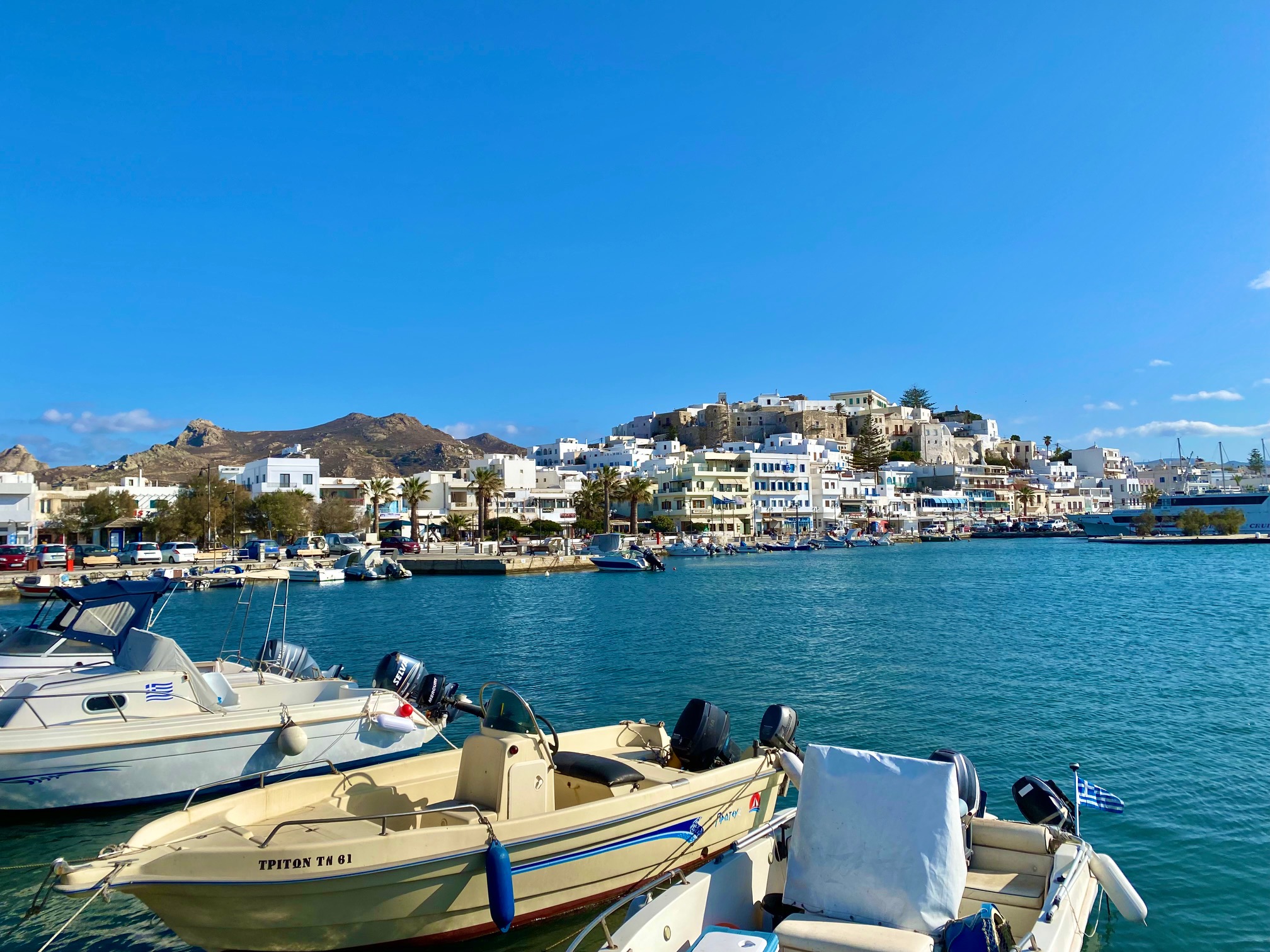 Small speedboats on turquoise water with a whitewashed town in the background | Naxos Greece - Naxos Travel Guide | greekislandbucketlist.com